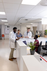 Happy diverse doctors and medical staff talking at reception desk of hospital ward, copy space