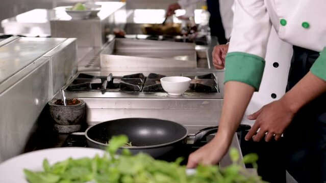 4K closeup hands working in kitchen, chef chopping vegetables tomatoes on table in restaurant, junior chef in cooking uniform stir veg in hot pan with smoke, multi-task in small business cuisine shop