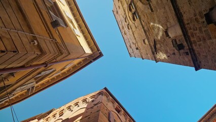 Looking up at the beautiful medieval architecture of the old city of Siena, Province of Siena, Italy. Handheld upward and orbit shot