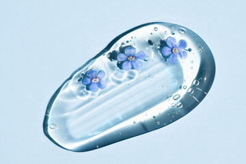 Smear of liquid peeling gel, transparent serum on a blue background with small flowers, macro.