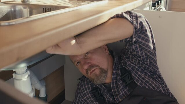 Mature Caucasian professional plumber with beard on face checking fixation of new sink in clients kitchen