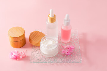 Obraz na płótnie Canvas A fashionable cosmetic product in glass matte white bottles and cream in a jar on a glass embossed tray and a pink background. natural cosmetics.