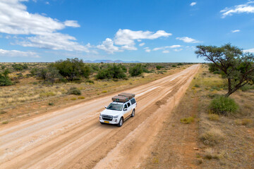 Drone image of offroad vehicle driving on dirt road in African bush - obrazy, fototapety, plakaty