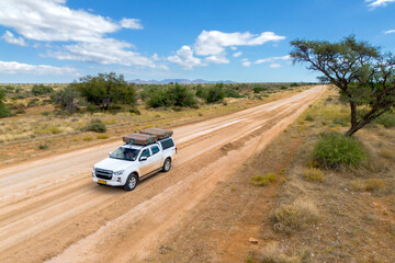Obraz na płótnie Canvas Drone image of offroad vehicle driving on dirt road in African bush
