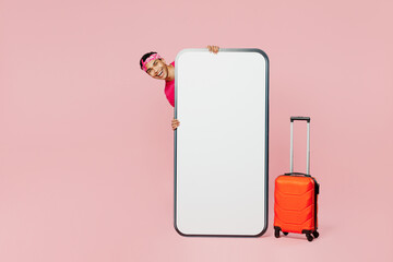 Traveler man wear casual clothes hold suitcase big huge blank screen mobile cell phone isolated on plain pink background. Tourist travel abroad in free spare time rest getaway Air flight trip concept