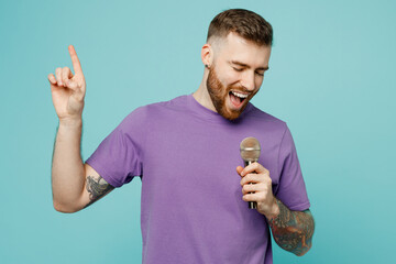 Young cheerful fun happy singer man he wears purple t-shirt sing song in microphone at karaoke club...
