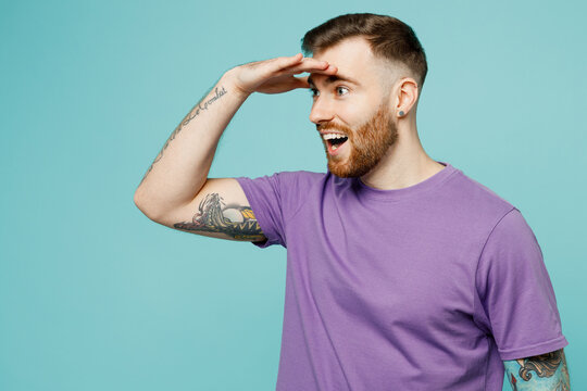 Side view young smiling happy man wear purple t-shirt hold hand at forehead look far away distance isolated on plain pastel light blue cyan background studio portrait. Tattoo translates life is fight