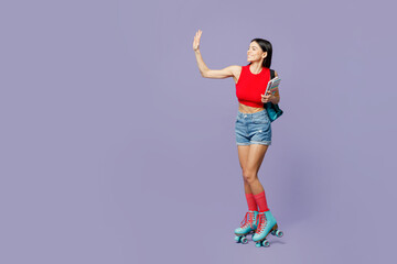 Full body student smiling fun young latin woman wear red casual clothes rollers backpack rollerblading waving hand hold books isolated on plain pastel purple background. Summer sport leisure concept.