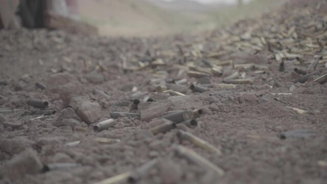 Giant bullet shell falling on the ground in slowmotion on sand that's covered in bullet shells on a shooting range in USA America LOG