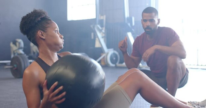 Diverse male coach motivating determined woman exercising with medicine ball at gym, in slow motion