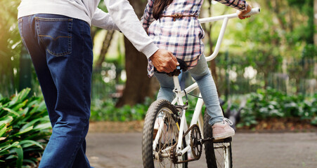 Father teaching his child to ride a bicycle on a path in an outdoor green community park. Love,...