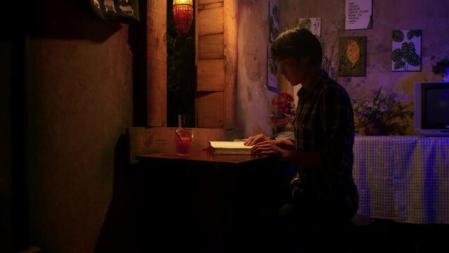 Close up of Asian young man reading a book at night in desk of small humble room