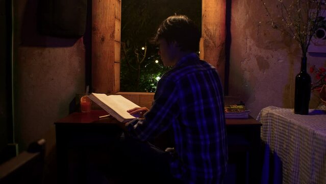 Back shot of a young Asian boy reading at night in his room.