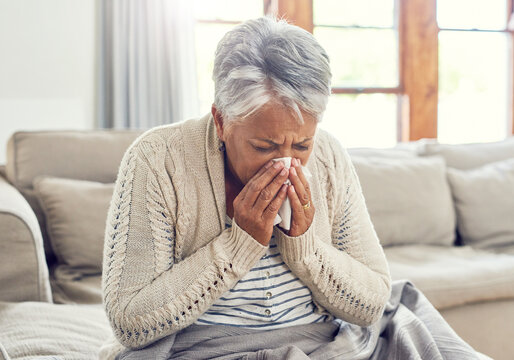 Senior woman, sick and blowing nose at home from virus, allergy and illness on couch. Tired, tissue and elderly female person in a house lounge with sneeze from covid and flu on a sofa with allergies