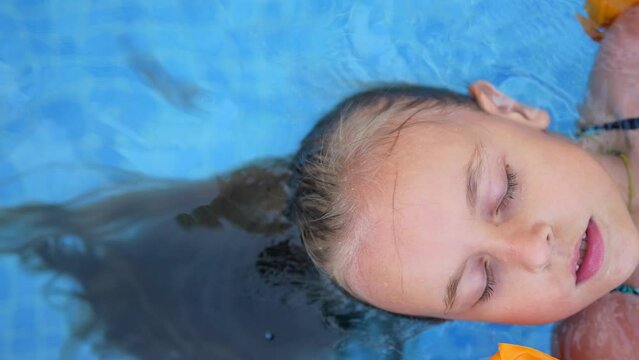 Little girl with closed eyes relaxing on back in the swimming pool, close-up