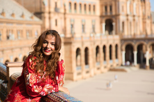 A beautiful young woman wearing a traditional Moroccan red dress with gold and silver embroidery is on vacation in Seville, Spain.