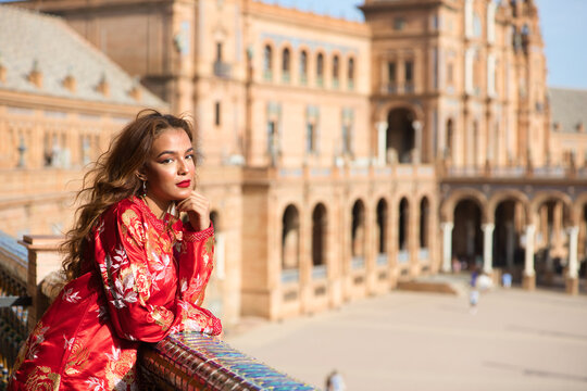 A beautiful young woman wearing a traditional Moroccan red dress with gold and silver embroidery is on vacation in Seville, Spain.