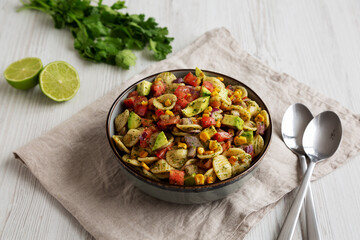 Homemade Grilled Corn Summer Pasta Salad in a Bowl on a white wooden background, low angle view.