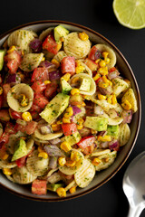 Homemade Grilled Corn Summer Pasta Salad in a Bowl on a black background, top view. Flat lay, overhead, from above. Close-up.