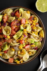 Homemade Grilled Corn Summer Pasta Salad in a Bowl on a black background, top view.