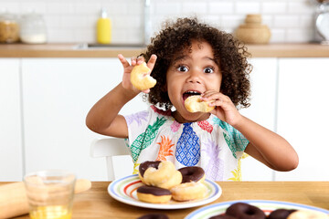 Young girl at kitchen table eating donuts with funny expression