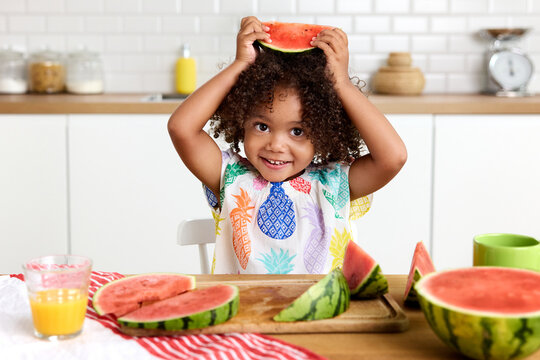 Cute toddler girl holding slice of watermelon above head