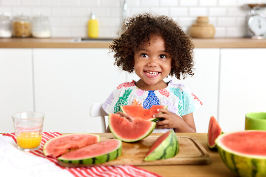 Happy preschooler at kitchen table holding watermelon slice