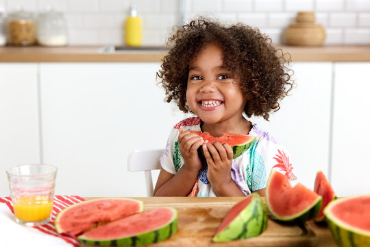 Happy preschooler at kitchen table eating watermelon