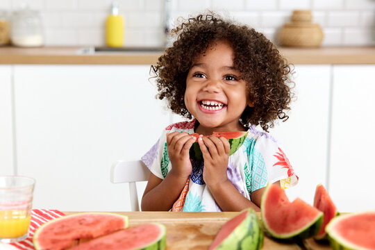 Laughing young girl at kitchen table eating watermelon