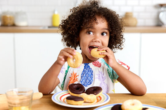 Happy toddler girl at kitchen table eating donuts