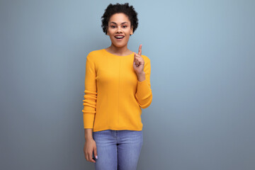 smart young latin woman with afro hair pointing finger to the side on gray background with copy space