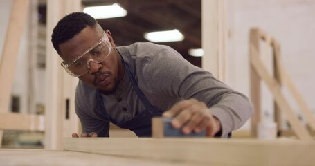 Carpentry, design and sandpaper with a black man in his factory to finish a professional woodwork project. Safety goggles, manual labor and expertise with a carpenter sanding in his creative workshop