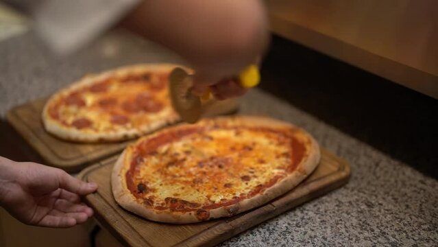Side view from above of anonimous pizzeria worker slicing deliciously looking tomato cheese pizza with cutter wheel in order to be served