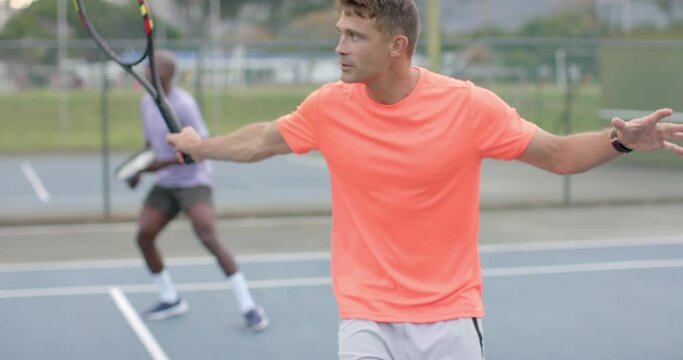 Two diverse male friends playing doubles returning ball on outdoor court in slow motion
