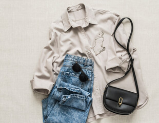 Women's comfort casual clothing - mom's blue jeans, cotton shirt, sunglasses, chain and cross body bag on a light background, top view