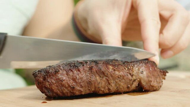 I cut a piece of beef steak in half with a knife on a wooden cutting board, close-up shot, medium doneness.