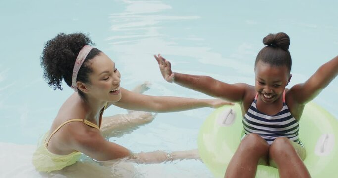 Portrait of african american mother and daughter playing in swimming pool in garden, slow motion