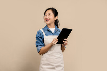 Beautiful asian waitress wearing brown apron work in coffee shop holding digital tablet and looking...