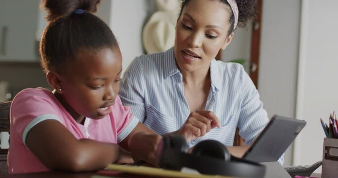 Happy african american mother and daughter using tablet and doing homework together, slow motion