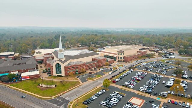 Distant drone shot of a mega church building that has a full parking lot near it.