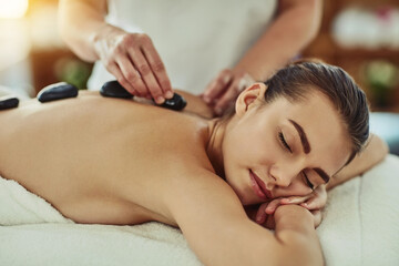 Spa, zen and woman getting a hot stone back massage for luxury, calm and natural self care. Beauty, body care and tranquil female person sleeping while doing a rock body therapy treatment at a salon.