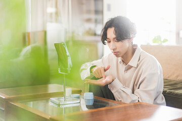 朝、リビングでヘアを整えている20代の日本人の一人暮らしの男性
