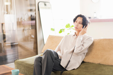 朝、リビングでヘッドフォンで音楽を聴いている20代の日本人の一人暮らしの男性
