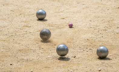 Fototapeta na wymiar Metal ball from the game of petanque approaching the red bowling alley bouncing off the sandy ground kicking up dust and grit from a petanque court on a sunny day