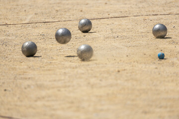 Metal ball from the game of petanque approaching the bowling ball bouncing on the sandy ground raising dust from a petanque court on a sunny day with the shadows of the trees on the ground