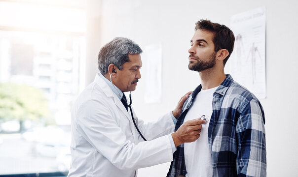 Healthcare, patient and doctor with stethoscope for checkup, help and wellness at hospital. Medicine, health care and heart expert with Indian man in doctors office consulting medical professional.