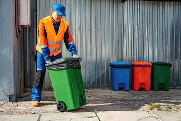 Male janitor in uniform cleans a trash can in the street