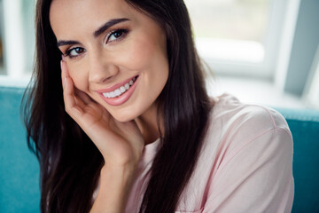 Close up cropped portrait of lovely cheerful person sitting sofa beaming smile hand touch cheek flat inside