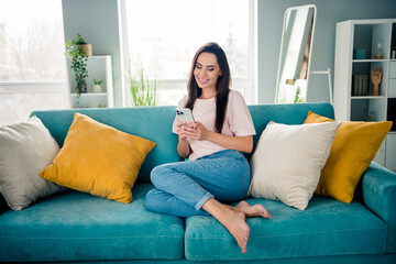 Full body portrait of pretty cheerful lady sitting comfort sofa use smart phone enjoy peaceful day apartment inside
