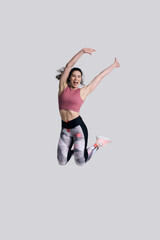 Fototapeta na wymiar Determined strong young sportswoman, smiling and raising arm while jumping high on white background.